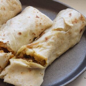 Three GRAB AND GO 4 OZ. New Mexico Burritos from two 2-packs, each with different fillings including meat and vegetables, are arranged on a round, dark plate.