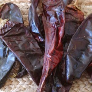 A close-up of several HATCH SUN DRIED CHILE PODS, CHOICE OF FLAVORS on a woven straw surface.