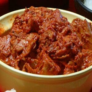 A bowl filled with CARNE ADOVADA spicy red pork stew, placed on a red surface.
