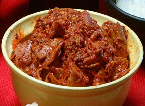 A bowl filled with CARNE ADOVADA spicy red pork stew, placed on a red surface.