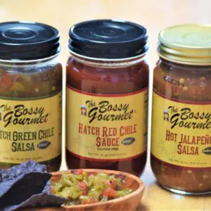 Image of three jars of Authentic New Mexico Salsas - Choice of Flavors: Hatch Green Chile Salsa, Hatch Red Chile Sauce, and Hot Jalapeño Salsa. Blue corn tortilla chips and a salsa dip are placed in front of the jars.
