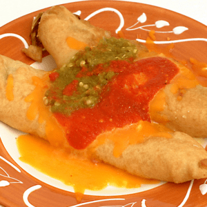 A plate featuring Chiles Rellenos, stuffed and fried tortillas topped with rich red and green salsa and melted cheese in the center. Package of four.