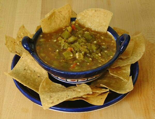 A serving of Salsa Fresca in a bowl, accompanied by tortilla chips on a wooden surface.