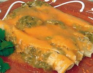 A dish of GREEN CHILE ENCHILADAS featuring three enchiladas topped with melted cheddar cheese and green salsa, garnished with cilantro, served on a decorative brown plate. our fresh corn tortillas are perfect for homemade enchiladas.