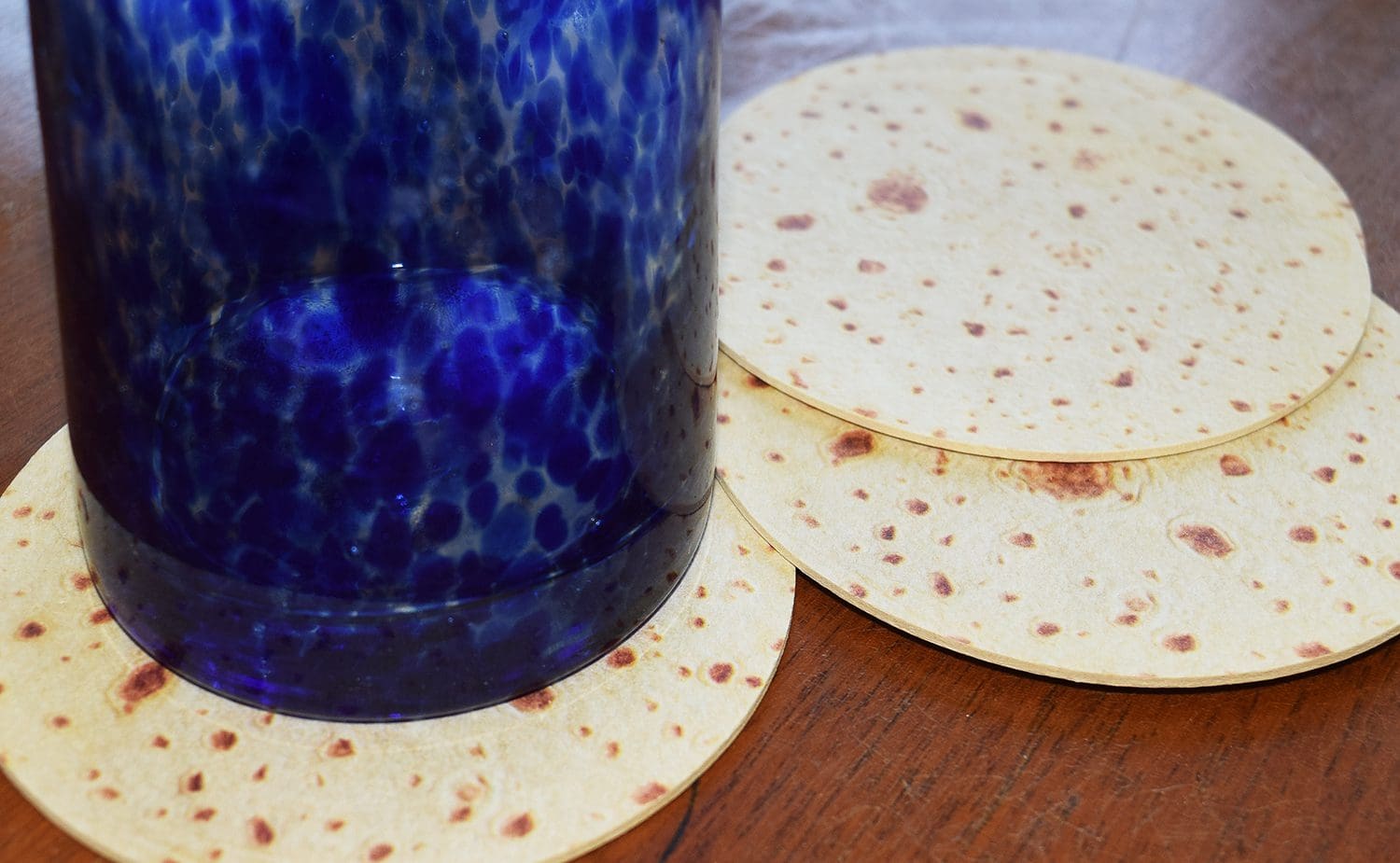Blue glass on a table with three Tortilla Beverage Coasters.