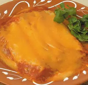 A plate of RED CHILE ENCHILADAS topped with melted cheese and garnished with a sprig of cilantro on a decorative orange plate.