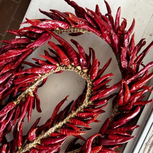 A string of ALL-NATURAL CHILE PEQUIN GARLAND arranged in a loop on a light-colored surface.