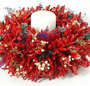 The CHILE PEQUIN CENTERPIECE features a white candle surrounded by a wreath made of red chili peppers, small white flowers, and green leaves.