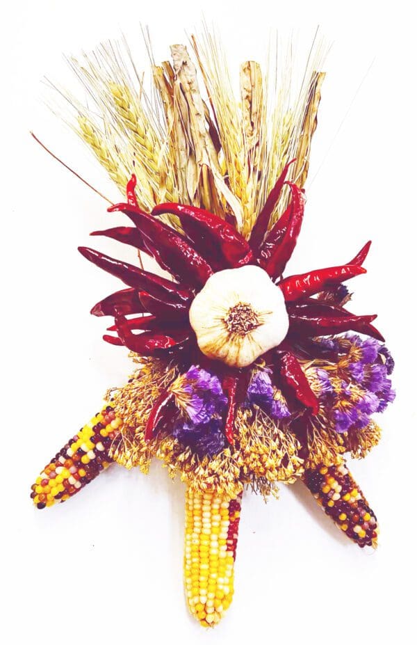 A decorative Chile Corn Ristra, measuring 7'' x 10'', featuring dried corn, red chillies, a garlic bulb, purple flowers, and wheat stalks.