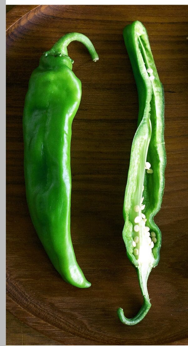 Two HOT SANDIA GREEN CHILES on a wooden surface: one whole and the other sliced open to reveal its seeds.