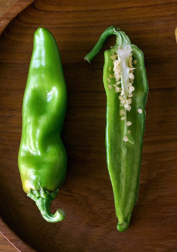Two EXTRA-HOT BARKER'S GREEN CHILES on a wooden surface: one whole and one sliced lengthwise showing seeds.