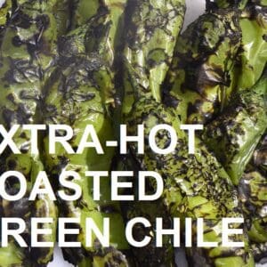 Close-up of several roasted green chiles with a charred appearance, overlaid with the text "EXTRA-HOT BARKER'S GREEN CHILE - ROASTED.