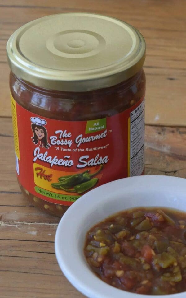A jar of salsa next to a bowl on the table.
