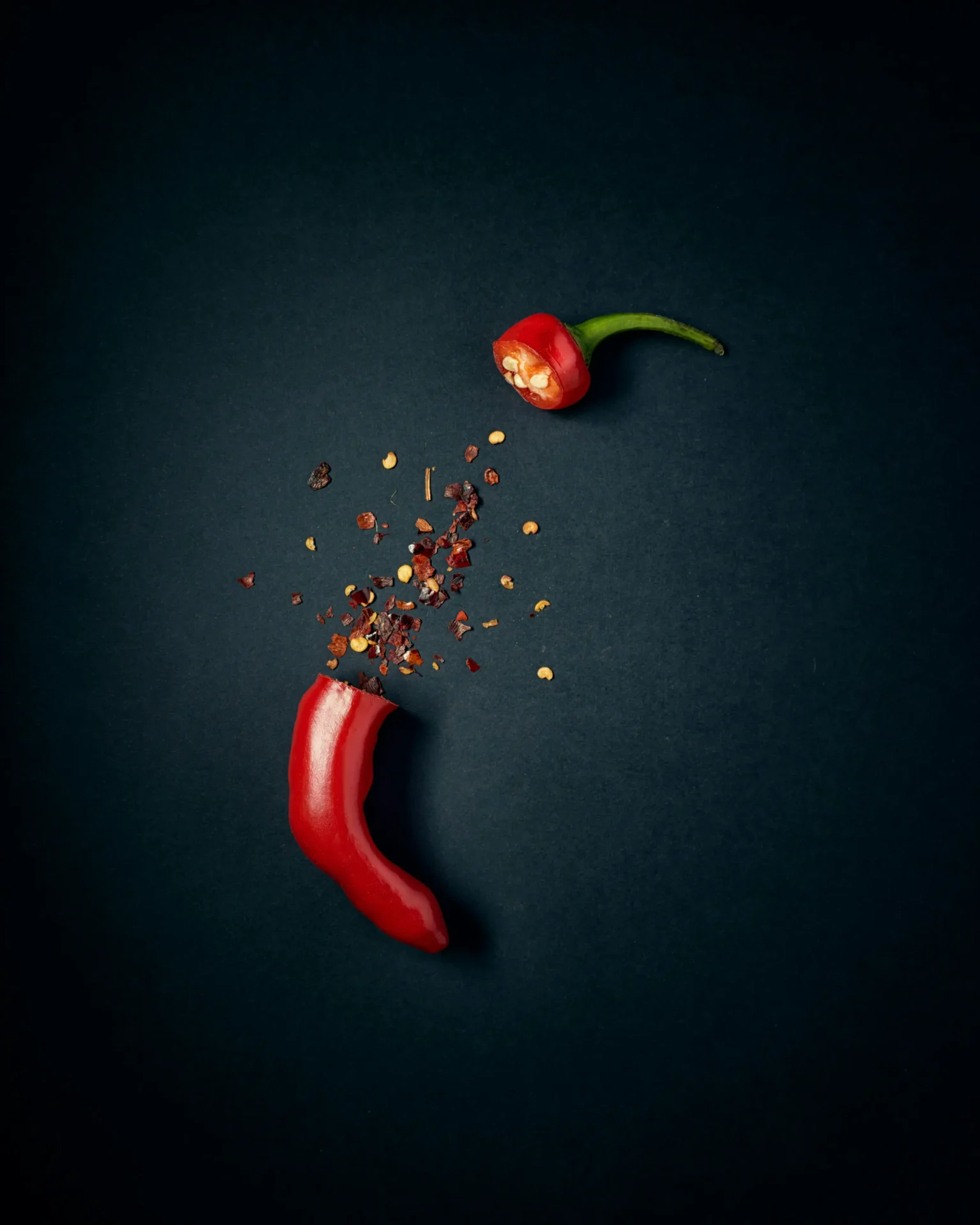 A red chili pepper is cut in half with seeds and flakes spilling out against a dark background, perfect for adding a kick to fresh salsas.