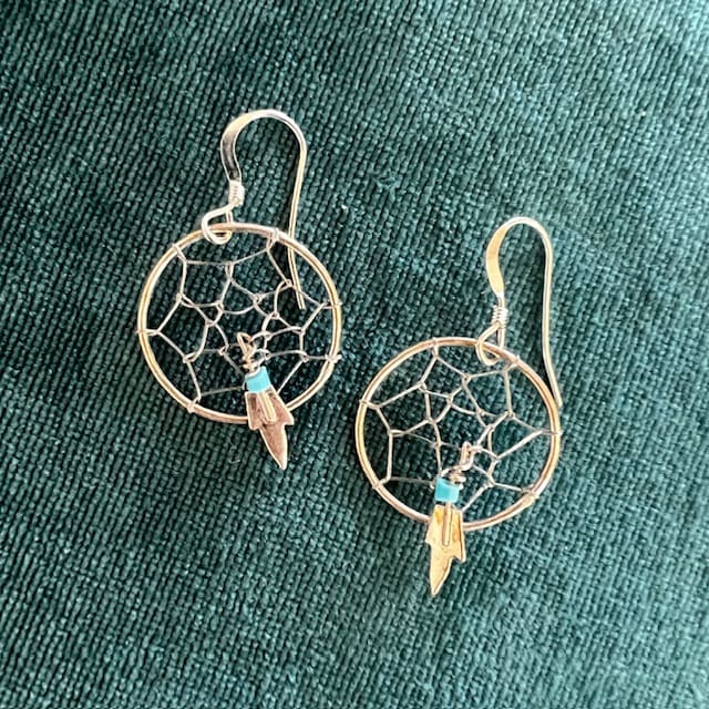 Silver dreamcatcher earrings with feather charms on a green fabric background.